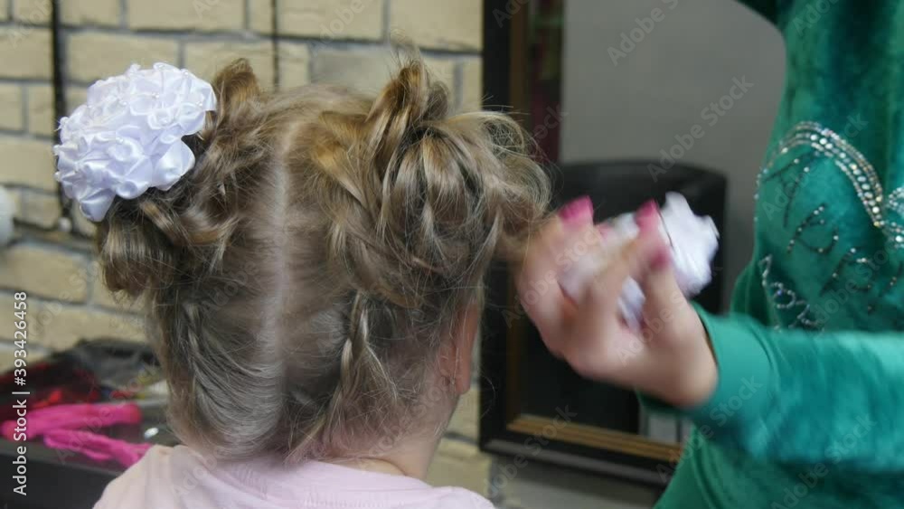 Process of creating a hairstyle from braiding braids for young girl in barbershop. Process of completing braiding braids with white bows on the head of a young girl in a Barber shop close - up. Process of creating a hairstyle from braiding braids for young girl in barbershop. Process of completing braiding braids with white bows on the head of a young girl in a Barber shop close - up.