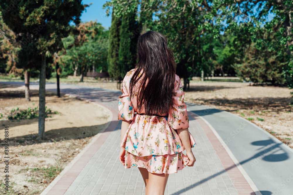 Beautiful brunette woman in a dress with flowers walks in the park alone Beautiful brunette woman in a dress with flowers walks in the park alone