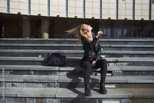 A woman in a leather jacket sits on the stairs near the theater on the street model