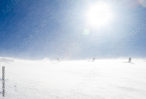 Snowstorm on a sunny day. Skiers go down the slope. Bad Gastein, Austrian Alps.