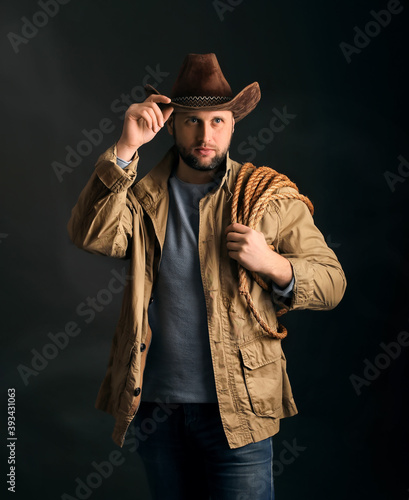 Cowboy in a hat and with a rope on his shoulder on a dark background © Denis