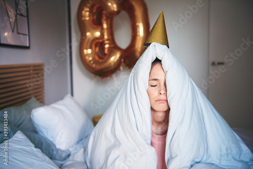 Sad woman celebrating her birthday, sitting on bed under blanket photo