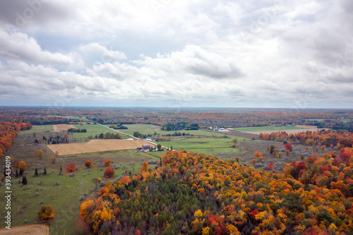 Beautiful fall aerial photograph of farm land and woods in upper Wisconsin during peak autumn colors with green tree leaves turning orange, yellow, and red and fluffy white clouds in the sky above.