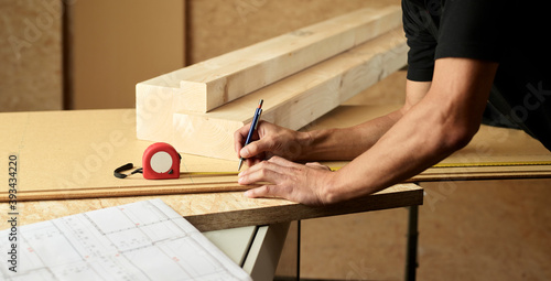Worker marking wood with pencil, tape measure