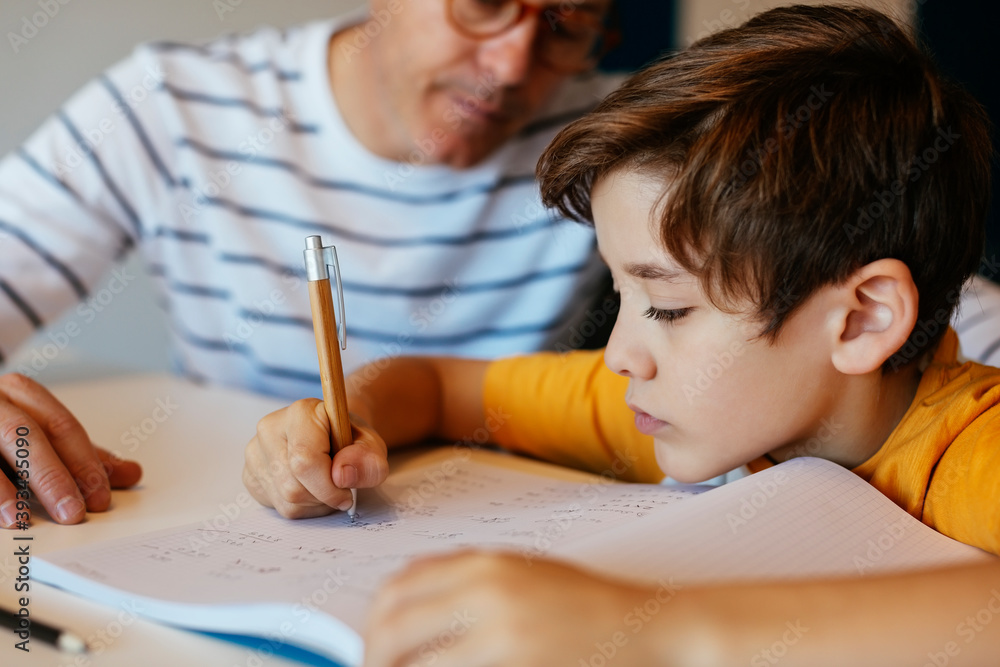 Father watching son doing homework at table Father watching son doing homework at table