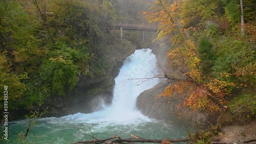 Raging waterfall in pristine nature, Vintgar gorge, Slovenia. Famous bridge over river Radovna. Colorful autumn landscape. Static shot, real time, wide angle