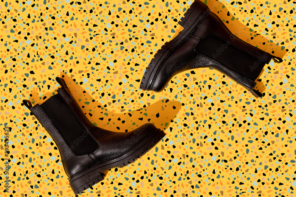 Pair of black leather boots on yellow terrazzo pattern