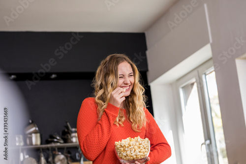 Portrait of giggling young woman with bowl of popcorn in the kitchen photo