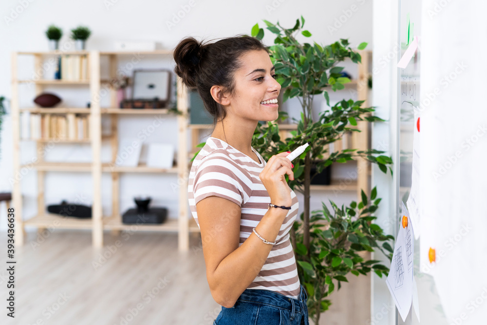 Smiling young businesswoman looking at whiteboard while working at office Smiling young businesswoman looking at whiteboard while working at office