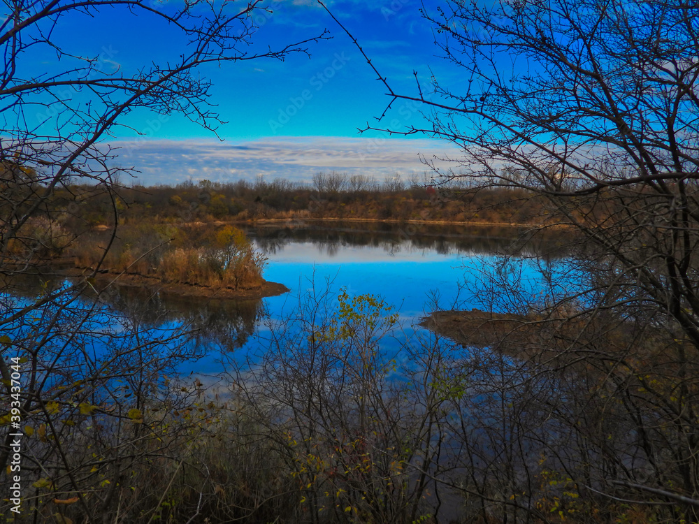 Obraz premium Reflection of trees in the water: Stunning and vibrant landscape view of a brilliant blue sky reflected in water in a late autumn landscape scenic view framed by bare tree branches