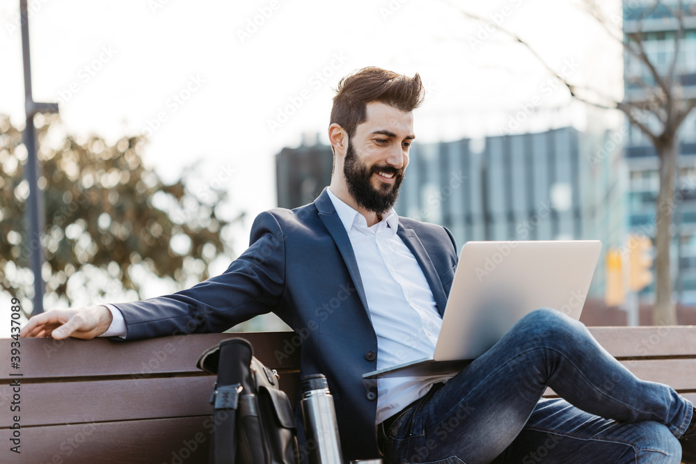 Businessman sitting on bench outside office building using laptop Businessman sitting on bench outside office building using laptop