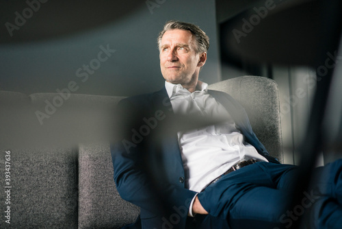 Mature businessman sitting on couch looking sideways photo
