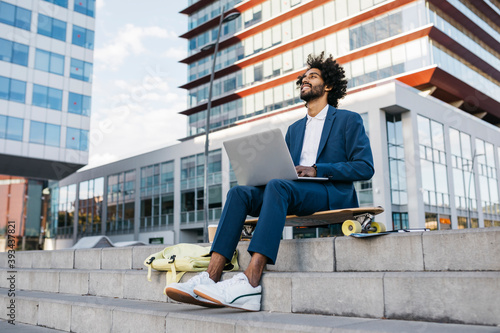 Spain, Barcelona, young businessman sitting outdoors in the city working on laptop