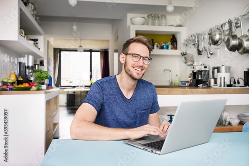 Portrait of smiling man using laptop in kitchen at home