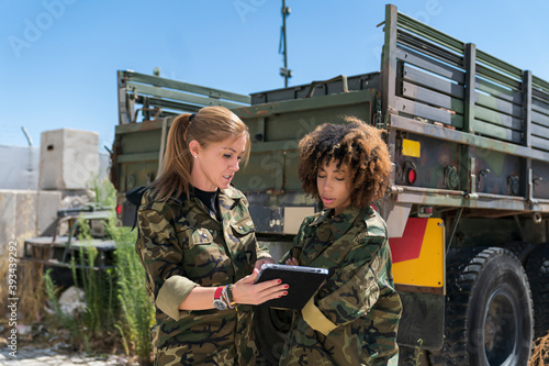 Multi-ethnic female army soldiers discussing over digital tablet at military base on sunny day