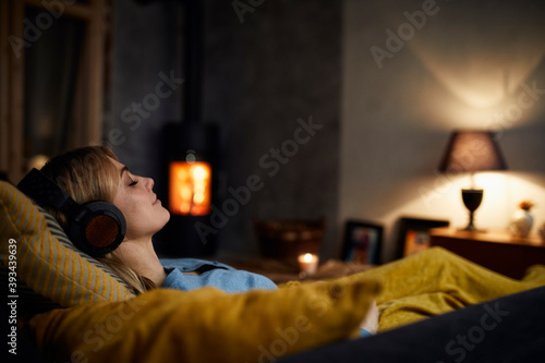 Smiling woman listening music with headphones on couch at home in the evening