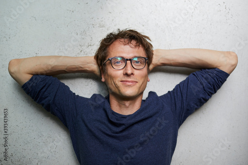 Portrait of smiling man with hands behind head wearing glasses photo