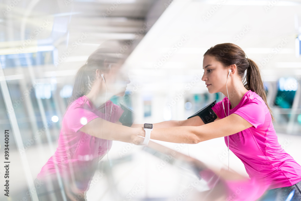 Young woman in pink sportshirt stretching and listening to music in modern urban setting