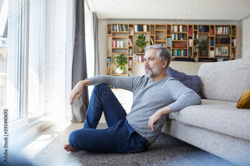 Mature man sitting on floor of his living room looking out of window photo