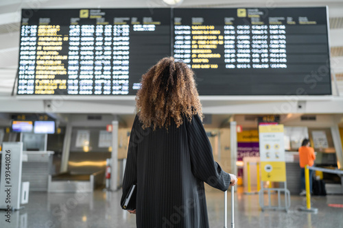 Young woman checking arrival timing of flight on board standing at airport photo