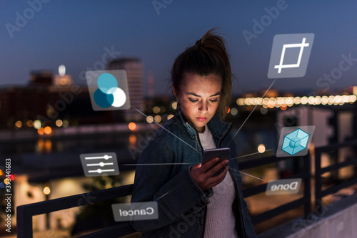 Young woman outdoors at night with data emerging from smartphone photo