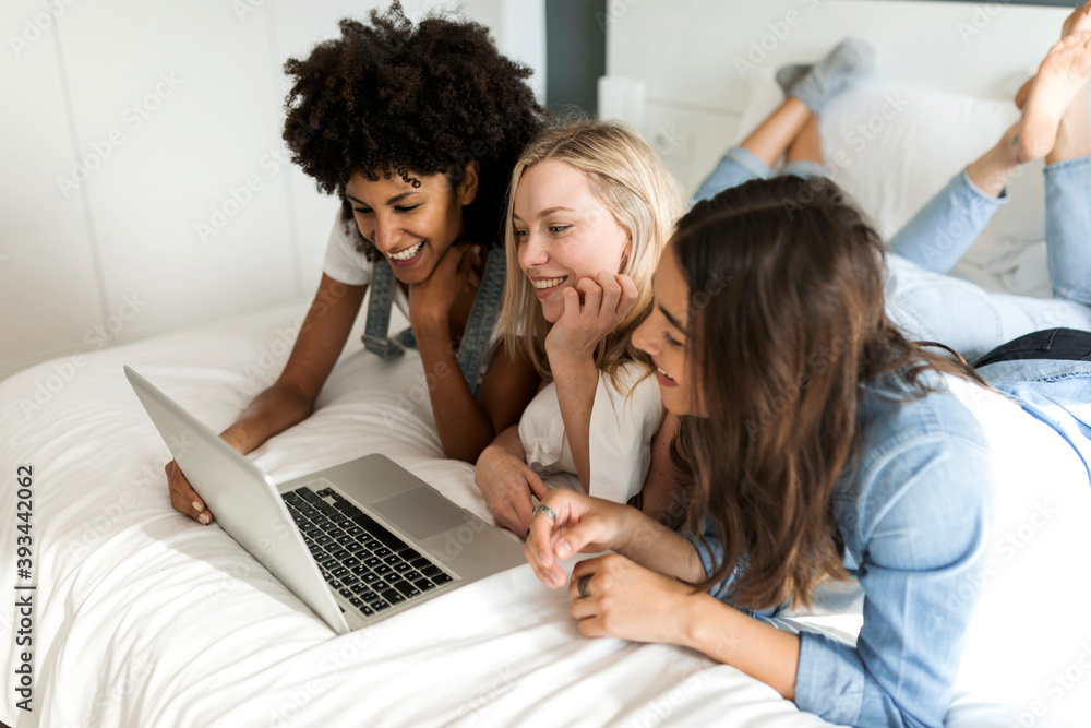 Three happy girlfriends lying on bed sharing laptop Three happy girlfriends lying on bed sharing laptop