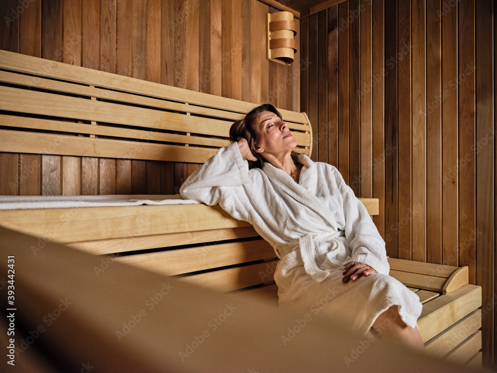 Senior woman with hands behind head relaxing in sauna at health spa Senior woman with hands behind head relaxing in sauna at health spa