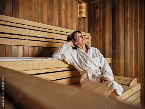 Senior woman with hands behind head relaxing in sauna at health spa