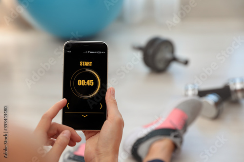 Young woman using fitness app on smartphone indoors, closeup. Space for text