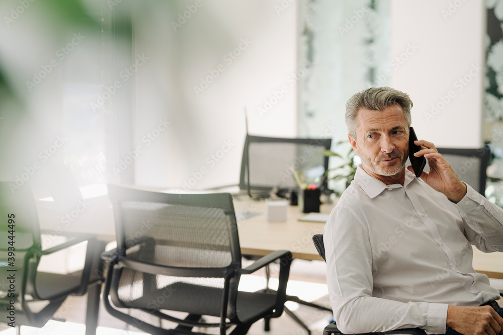 Businessman talking on phone while sitting on chair at office