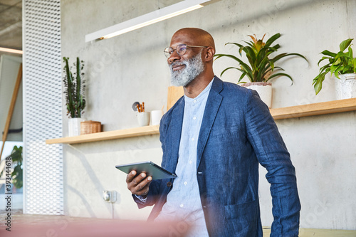 Smiling man looking away while holding digital tablet standing at home photo