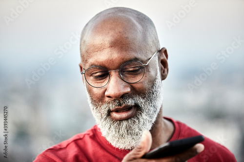 Bald man with white beard talking through mobile phone at building terrace during sunset