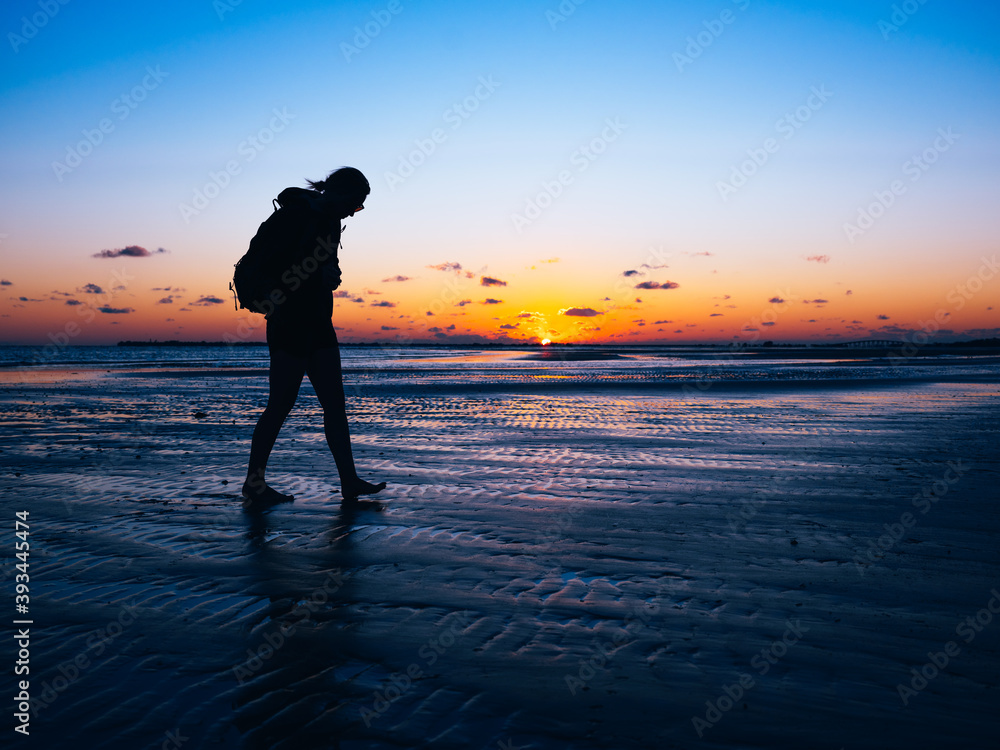Silhouette of girl walking on shallow water sand bank at sunset with room for copy