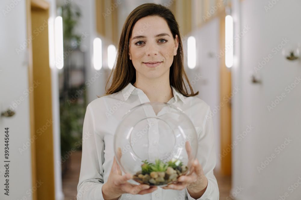 Smiling woman holding terrarium pot in hand while standing at office Smiling woman holding terrarium pot in hand while standing at office