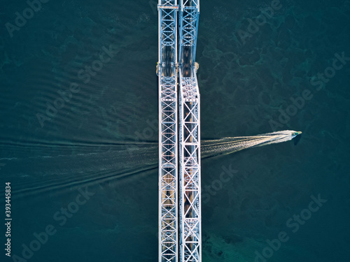 Aerial view of boat moving over Volga River under metallic railway bridge