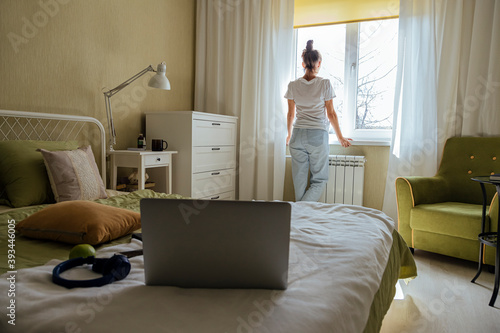 Mid adult woman looking out of window while standing in bedroom