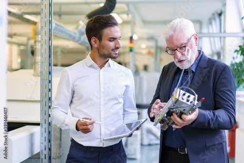 Senior manager discussing machine part with young male engineer at factory photo