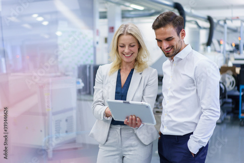 Smiling blond businesswoman discussing over digital tablet with young male colleague at factory photo