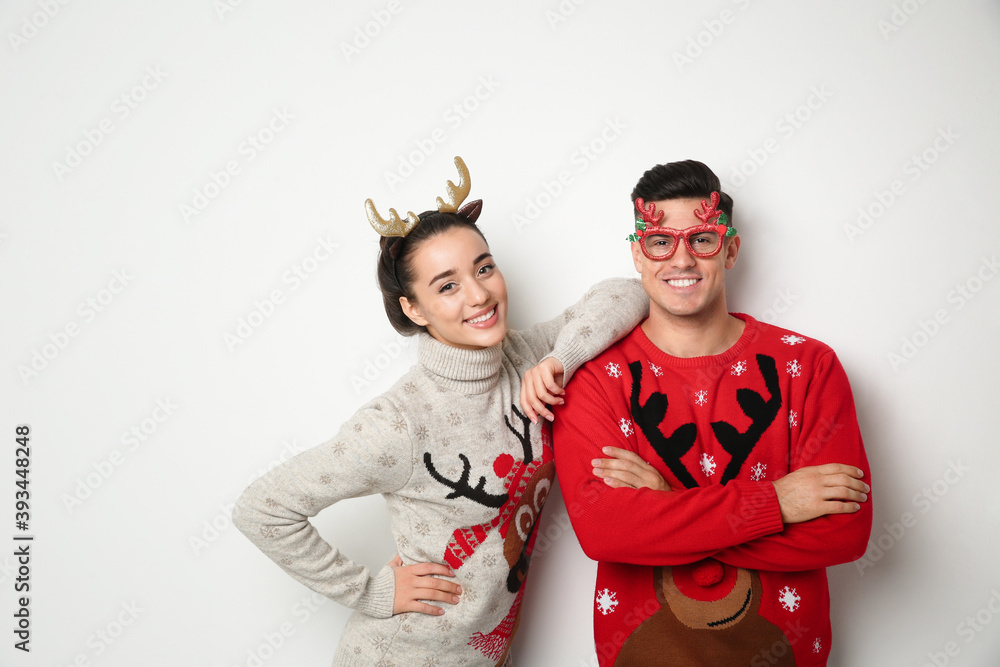 Couple in Christmas sweaters, deer headband and party glasses on white background