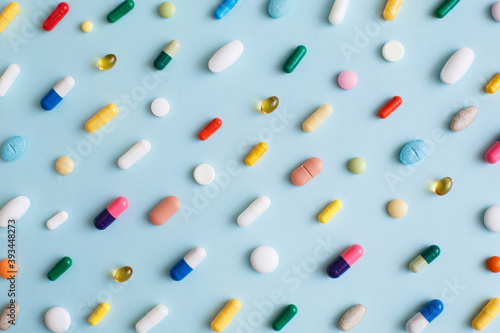 Creative layout of colorful pills and capsules on blue background. Minimal medical concept. Pharmaceutical, Covid-19 or Coronavirus. Flat lay, top view photo