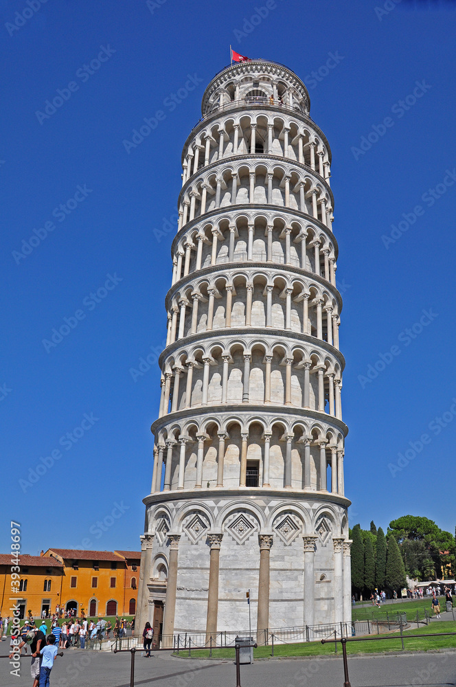 The Leaning Tower of Pisa seen from the ground level. The tower has both symmetry and intricately woven elements of arches and columns accenting its unique beauty.