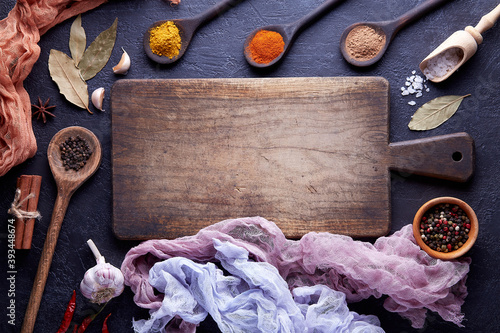 Cutting board with spices and herbs for cooking meat on dark background