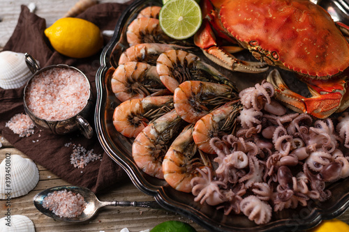 Dish with assorted seafood. Cooked crab, baby octopuses and tiger shrimps served with lime, lemon, sea salt and seashells on rustic wooden background. Seafood concept. Delicious meal.