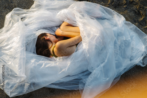 The girl is wrapped in plastic film and lies on the black sand on the beach photo