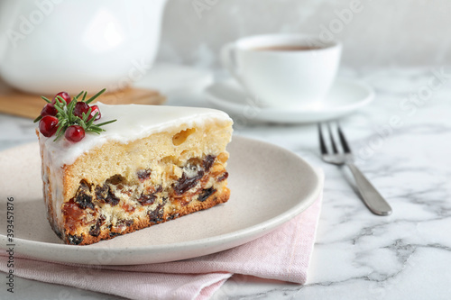 Slice of traditional Christmas cake decorated with rosemary and pomegranate seeds on white marble table
