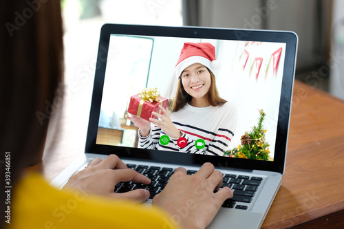 Asian girl make video call while holding gift box and greeting in Christmas holiday celebration by laptop computer, new normal, online party celebrating, telecommunication