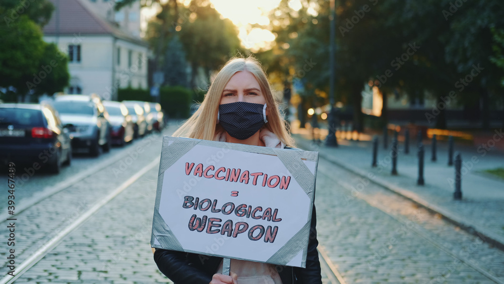 Young woman protesting against vaccination like biological weapon. She worn protective mask and walking down the street
