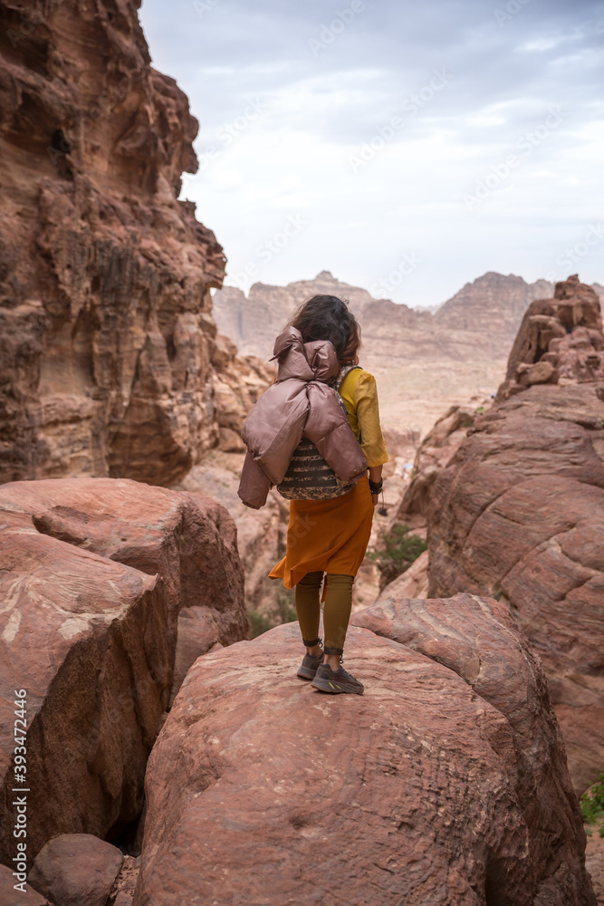 A tourist girl in a yellow shirt and a backpack stands on a rock and prepares to go down