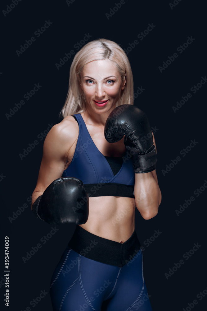 Cute blonde in boxing gloves smiles and prepares for training isolated on black background