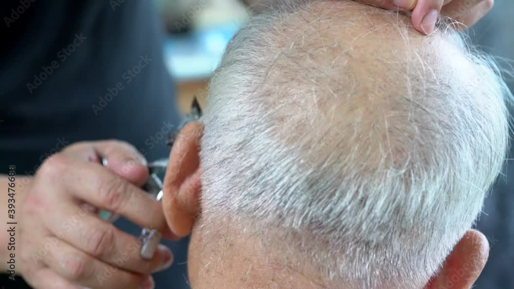 The barber is cutting the hair of an old man with gray hair The barber is cutting the hair of an old man with gray hair